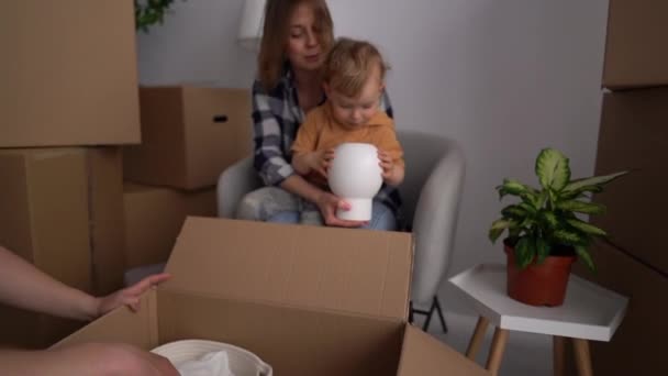 Счастливая семья с маленьким ребенком распаковывает коробки в новой квартире. Концепция недвижимости и ипотеки — стоковое видео