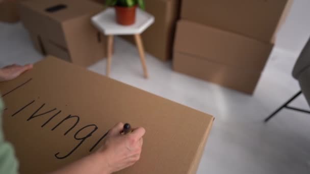 Close portrait of a young man writing on cardboard boxes labeling them for moving out, copy space. Livingroom lettering, attempts to streamline space, minimalism concept. 4K — Stock Video