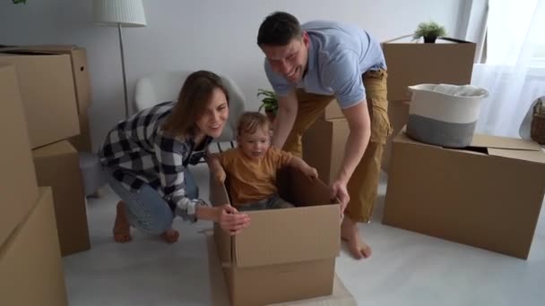 Immobili e ipoteca concetto. Giovane famiglia felice in una nuova casa rotola il loro bambino in una scatola di cartone sul pavimento — Video Stock