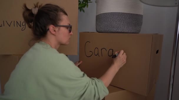 Nahes Porträt einer Frau, die Dinge in Kartons verpackt und signiert. Umzug, neuer Wohnort und Minimalismus-Konzept — Stockvideo