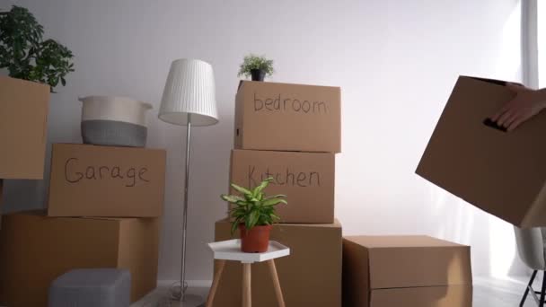 Stěhování, přemísťování a minimalismus. Žena přináší lepenkové krabice s nápisy garáž, kuchyň, obývací pokoj, ložnice, koupelna do svého nového domova — Stock video