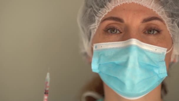 Porträt einer Krankenschwester mit Maske, Schutzmütze und Brille. Frau hält Spritze mit Covid-19-Impfstoff in der Hand — Stockvideo