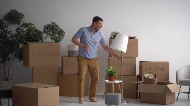 Minimalisme en decluttering. Een volwassen man brengt dozen met dingen in een nieuw huis en danst tegen de achtergrond van gesigneerde dozen. Concept vastgoed en hypotheek — Stockvideo