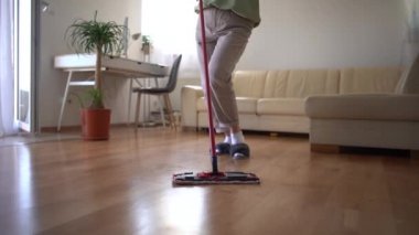 Temizlik sırasında şarkı söyleyen, paspasla dans eden ve kulaklıkla müzik dinleyen bir kadın. Güzel ev hanımı temizlik yaparken eğleniyor, ağır çekimde.