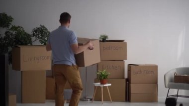 Yetişkin bir erkek yeni bir eve kutular dolusu şey getirir ve imzalı kutuların arkasında dans eder. Emlak ve ipotek konsepti. Minimalizm ve azalma