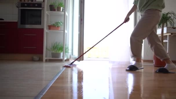 Een vrouw met een koptelefoon is de vloer aan het wassen met dweilen en dansen thuis. Grappige jonge dame heeft plezier tijdens het opruimen zingen en dansen met dweilen genieten van muziek in koptelefoon — Stockvideo