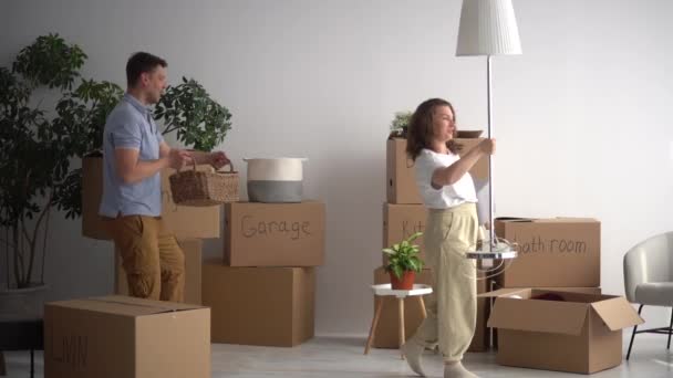 Manžel a manželka balí věci do lepenkových krabic s nápisy obývací pokoj, koupelna, kuchyň. Šťastný manželský pár bavit a tanec při stěhování do svého nového majetku — Stock video