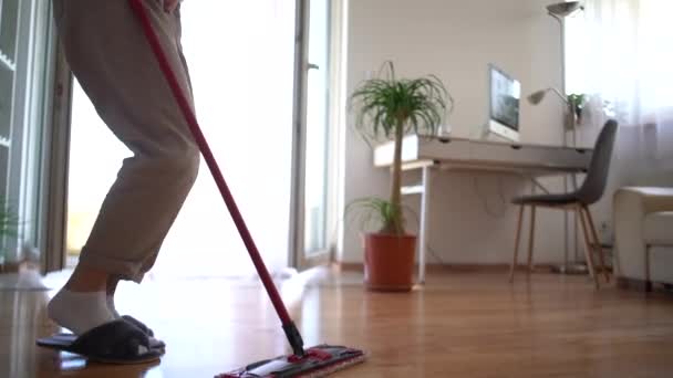 Happy housewife mops the floor and sings while listening to music on wireless headphones. House cleaning, weekend at home concept — Stock Video