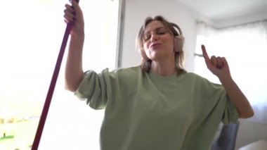 Yerleri paspaslarken dans eden ve şarkı söyleyen çekici bir ev kadınının yakın portresi. Ev temizliği, temizlik yapan kadınlar.