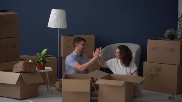 Чоловік і дружина закінчують упаковку для переїзду. Хіт один одному руки і покласти картонні коробки з обличчями, намальованими на них на голові — стокове відео