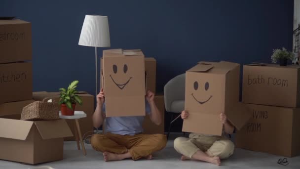 Husband and wife finish packing for the move. Hit each others hands and put cardboard boxes with faces painted on them on their heads — Stock Video