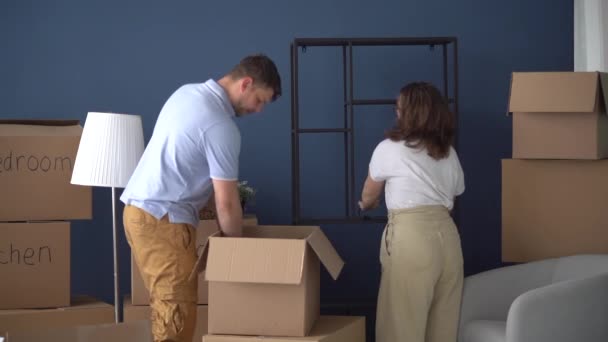 Man en vrouw, een gelukkig gezin, huiseigenaren die dingen uitpakken uit kartonnen dozen in een nieuw huis. Vastgoed- en woningkoopconcept — Stockvideo