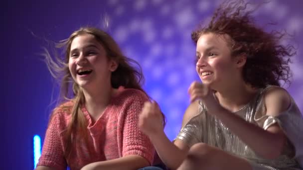 Festligt festkoncept. Porträtt av två tonårsflickor med att utveckla hår mot bakgrund av neonljus. Disco fest i nattklubben kreativ video — Stockvideo