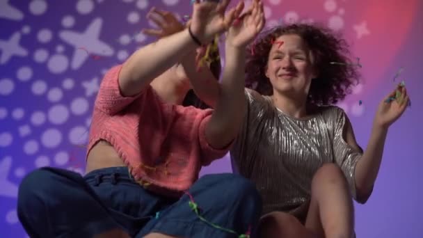 Impreza urodzinowa w stylu disco. Neonowe światło, portret dwóch dziewczyn z latającymi włosami w nocnym klubie, konfetti i iskry lecące na ich twarzach — Wideo stockowe