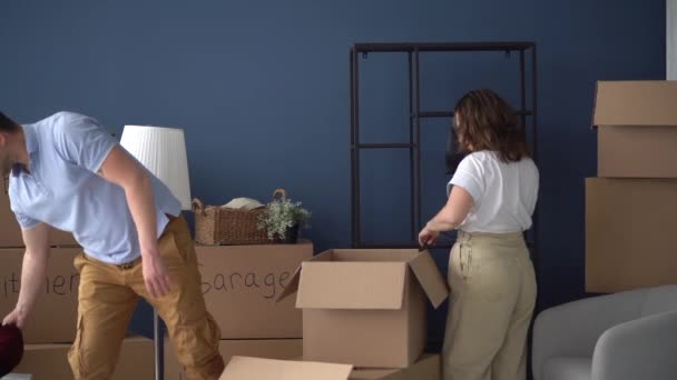 Marido e mulher, um casal feliz desempacotar caixas de papelão com coisas. Mudando-se para uma nova casa, os recém-casados equipar sua casa — Vídeo de Stock