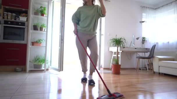 Szczęśliwa kobieta lubi myć podłogi słuchając muzyki na słuchawkach. Dojrzałe lady jest sprzątanie jej dom — Wideo stockowe