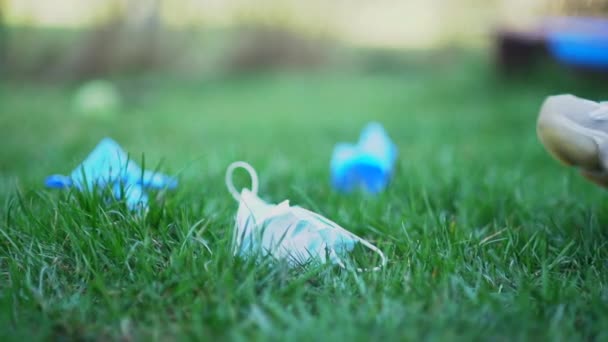 Covid-19 en de gevolgen voor het milieu. Close-up van een onherkenbare vrouw verzamelt gebruikte maskers en handschoenen in het park op het gras. Milieuverontreiniging met persoonlijke beschermingsmiddelen — Stockvideo