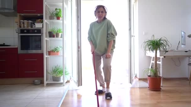 Poland, Wroclaw - March 30, 2021. Mature lady is cleaning her house. Happy woman enjoying mopping floors while listening to music on her headphones — Stock Video