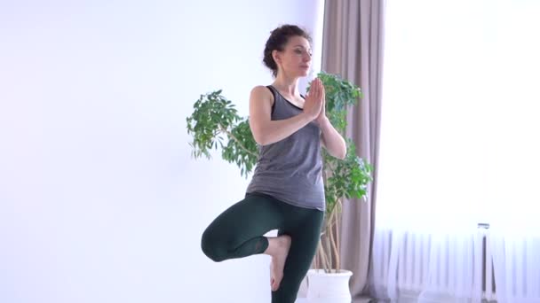 Dorosła kobieta ćwiczy jogę w studiu jogi. Dziewczyna w odzieży sportowej balansowanie w pozycji drzewa, uważność i koncepcja medytacji — Wideo stockowe