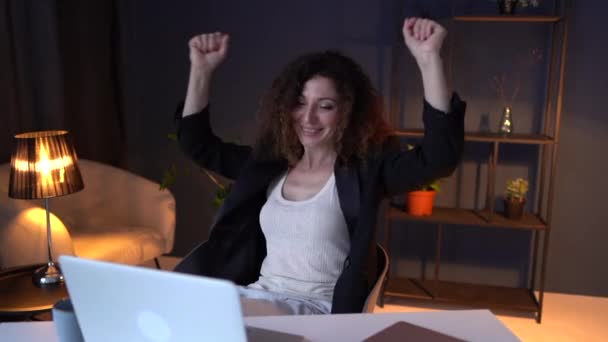 Een mooie volwassen zakenvrouw in een zakenpak danst terwijl ze in een werkstoel naast een laptop zit. Vrouw luistert naar manlief en geniet op het werk — Stockvideo