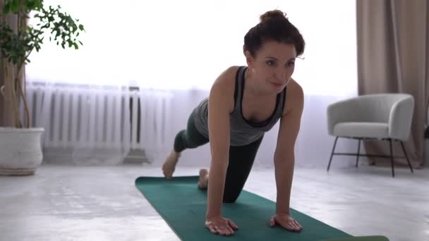 Mooie brunette is thuis aan het trainen op een yoga mat. Het meisje doet oefeningen voor de spieren van de benen en rug. Thuis workout fitness activiteit — Stockvideo