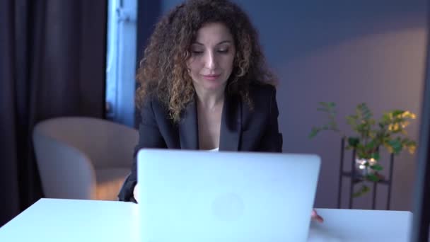 Η επιχειρηματίας δουλεύει στο γραφείο. Άνετος χώρος εργασίας. Ελκυστική σγουρή γυναίκα στην επιχείρηση δακτυλογράφηση κοστούμι στο πληκτρολόγιο laptop — Αρχείο Βίντεο