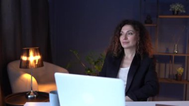 Ofiste dizüstü bilgisayarla çalışırken gülümseyen bir kız. Yetişkin çekici esmer iş kadını defterini kullanarak sohbet ediyor.