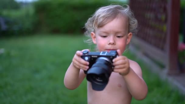 Small inquisitive three-year-old boy holds a professional camera with a lens in his hands. Little photographer, future videographer — Stock Video