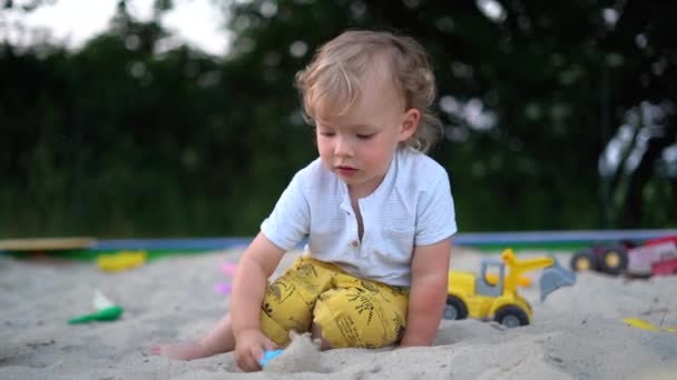 Портрет милого очаровательного блондина с игрушками для песка на фоне природы. Обаятельный застенчивый ребенок на открытом воздухе. Детство, семья и летняя концепция — стоковое видео
