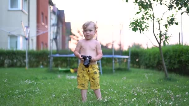 Le petit enfant joue avec une caméra vidéo professionnelle dans la cour arrière. Loisirs et concept de traitement, choix de profession — Video