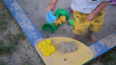 Plastik bir kalıp kullanarak kum boncuğu yapan bir çocuğun üst görüntüsü. Çocuk kum havuzunda oynuyor, yaz tatili konsepti.