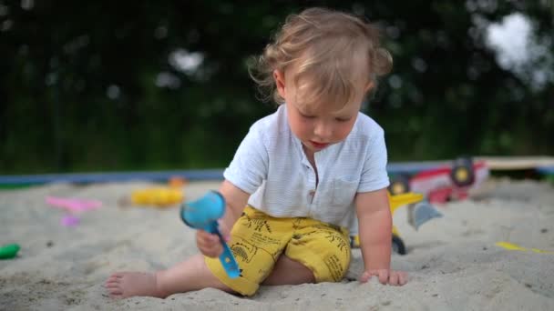 Обаятельный застенчивый ребенок на открытом воздухе. Портрет милого очаровательного блондина с игрушками для песка на фоне природы. Детство, семья и летняя концепция — стоковое видео
