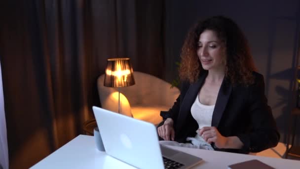 Красива бізнес-леді в чорному діловому костюмі працює пізно в офісі, танцює за столом біля ноутбука, насолоджується своєю роботою — стокове відео