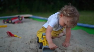 Küçük çocuk zamanını kum havuzunda geçirir ve plastik bir çöp kamyonu tutar. Yaz tatili, aile tatili
