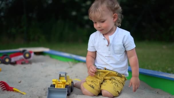 孩子们用塑料玩具在沙盒里挖沙子.敏锐的小男孩在玩一辆塑料垃圾车 — 图库视频影像
