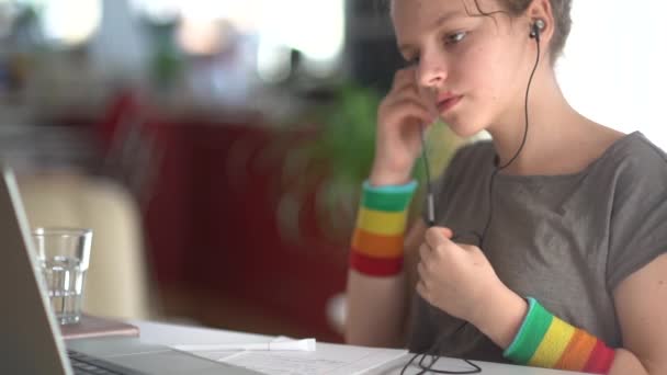 Concepto de aprendizaje en línea. La colegiala estudia en casa usando un portátil y auriculares. Tiene un bolígrafo en la mano. Concepto de aprendizaje electrónico y educación en el hogar — Vídeos de Stock