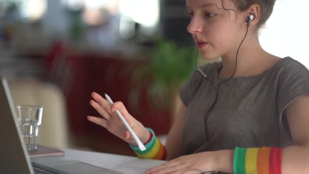 Eラーニングとホームスクーリングの概念。オンライン学習の概念。女子高生はノートパソコンやイヤホンを使って自宅で勉強します。手にペンを持って — ストック動画