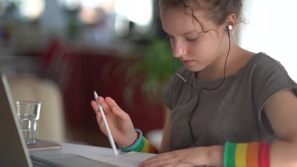 Teen ragazza lavora a casa con un computer portatile utilizzando cuffie cablate. Concetto di apprendimento online e homeschooling — Video Stock