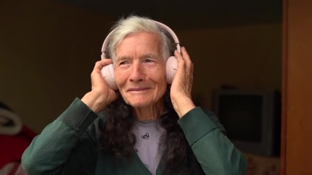 Staruszka używa bezprzewodowych słuchawek. Stara osoba i technologie. Wiejski emeryt, słucha muzyki ze słuchawkami bezprzewodowymi. Szczęśliwej emerytury, ludzie i gadżety — Wideo stockowe