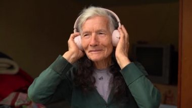 Yaşlılar ve teknolojiler. Köy emeklisi, kablosuz kulaklıkla müzik dinliyor. Mutlu emeklilik, insanlar ve aletler. Yaşlı kadın kablosuz kulaklık kullanıyor.