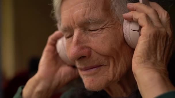 Donna anziana allegra che ascolta musica con grandi cuffie wireless rosa. Melomano pensionato positivo che ascolta musica. La bisnonna moderna — Video Stock