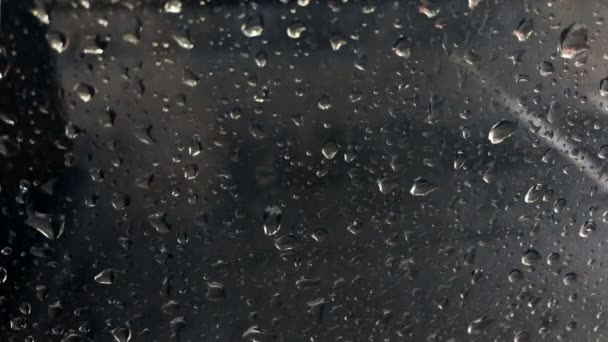 Gotas de lluvia cayendo en la ventana sobre un fondo oscuro neutro borroso por la noche — Vídeos de Stock