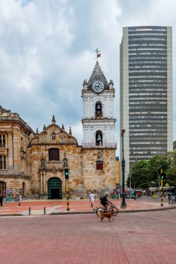 Beyaz saat kulesi olan tarihi taştan kilise, 9 Şubat 2025 tarihinde arka planda modern Torre Colpatria tarafından çerçevelenmiş Bogota kavşağında duruyor..