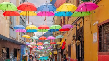 Bogota, Kolombiya 13 Şubat 2025 La Candelaria tarihi bölgesinde dar bir caddenin üzerinde asılı duran renkli şemsiyeler, yayaların şehir merkezinde sömürge döneminden kalma binalar arasında yürüdükleri yer..