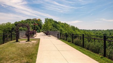 Aziz Thomas Ontario Kanada. 15 Haziran 2025: Ziyaretçiler, güneşli bir yaz gününde halka açık sanat manzarası ve yeşil manzaralı eski bir demiryolu koridoruna inşa edilen Yükseltilmiş Park yaya köprüsünün ve yürüyüş yolunun keyfini çıkarıyorlar..