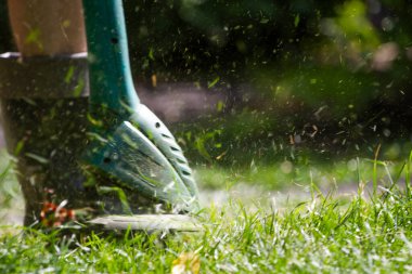 Bir adam çimleri biçme makinesiyle biçiyor.