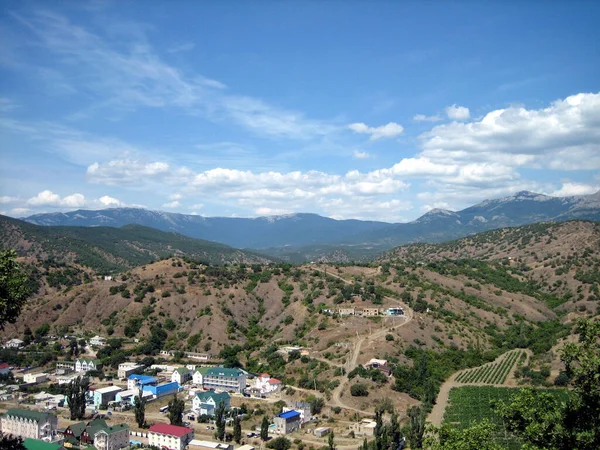 一个村庄 在风景如画的山谷里有房子和花园 四周环绕着小山 山坡上生长着树木 云彩飘扬在天空中 — 图库照片