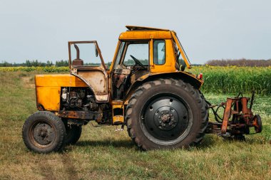 Paslı sarı bir traktör yeşil bir alanda duruyor. Öğleden sonra mısır tarlasında değil.