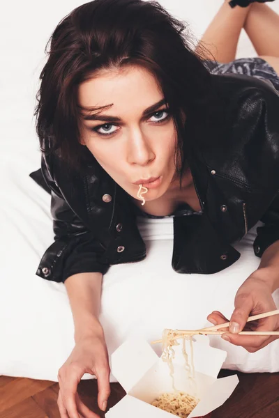 Sexy joven mujer acostada en la cama y comiendo fideos — Foto de Stock