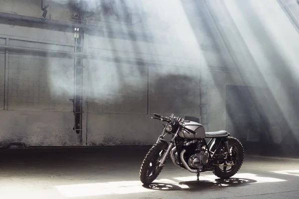 Moto debout dans le bâtiment sombre dans les rayons du soleil — Photo